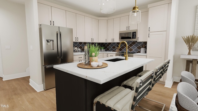 kitchen with decorative light fixtures, a kitchen island with sink, stainless steel appliances, and light hardwood / wood-style flooring