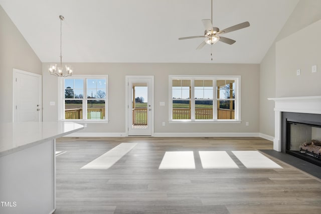 unfurnished living room with ceiling fan with notable chandelier, high vaulted ceiling, and light hardwood / wood-style flooring