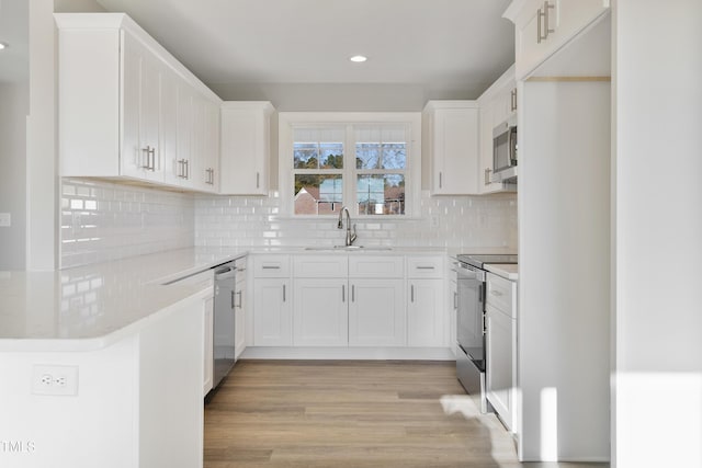 kitchen with white cabinetry, sink, light hardwood / wood-style floors, decorative backsplash, and appliances with stainless steel finishes