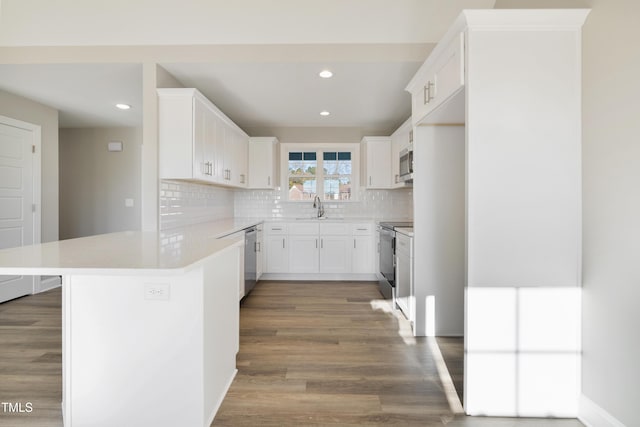 kitchen with kitchen peninsula, appliances with stainless steel finishes, sink, white cabinets, and hardwood / wood-style floors