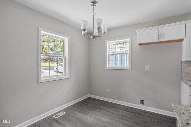 unfurnished dining area featuring dark wood-type flooring, a notable chandelier, and a healthy amount of sunlight