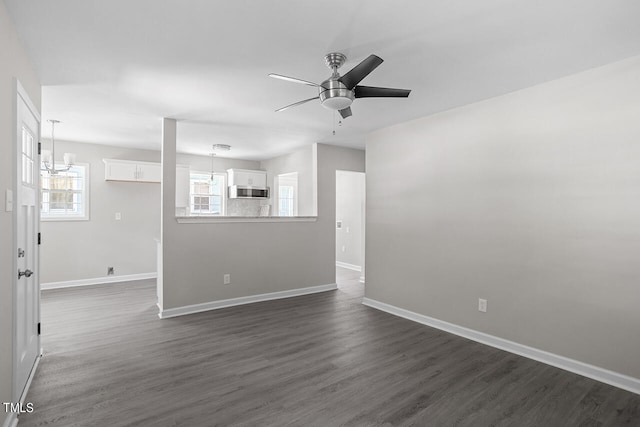 unfurnished living room featuring ceiling fan with notable chandelier, plenty of natural light, and dark wood-type flooring