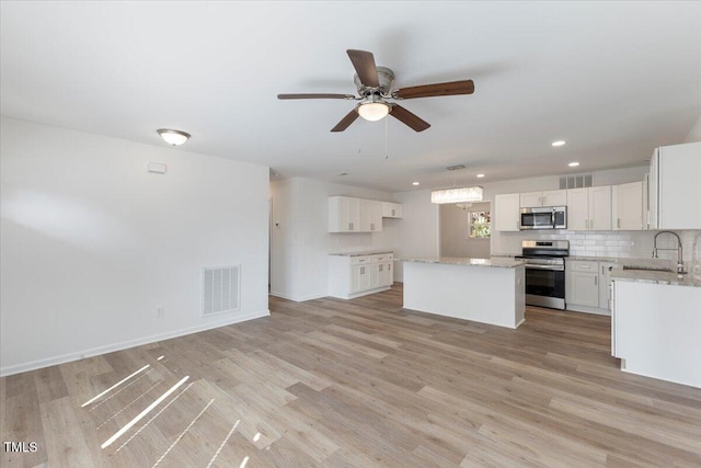 kitchen featuring stainless steel appliances, white cabinets, sink, a kitchen island, and light wood-type flooring