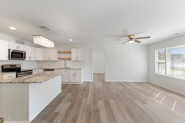 kitchen with light hardwood / wood-style floors, white cabinets, ceiling fan, light stone countertops, and appliances with stainless steel finishes