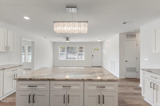 kitchen with white cabinetry, hanging light fixtures, light stone counters, and light hardwood / wood-style flooring