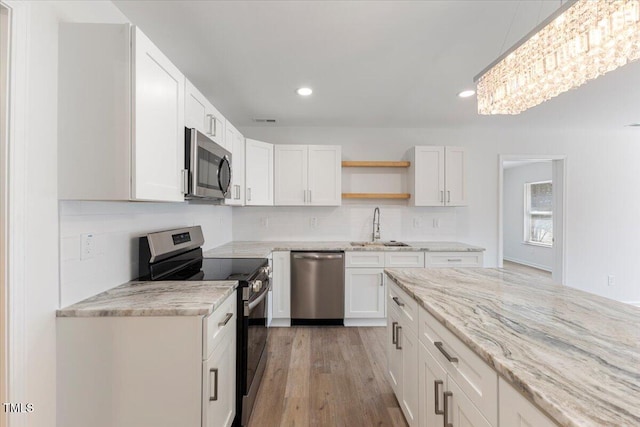 kitchen with stainless steel appliances, sink, tasteful backsplash, white cabinets, and light wood-type flooring