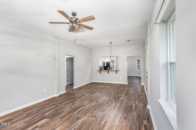 unfurnished living room featuring a textured ceiling, a healthy amount of sunlight, dark wood-type flooring, and ceiling fan with notable chandelier