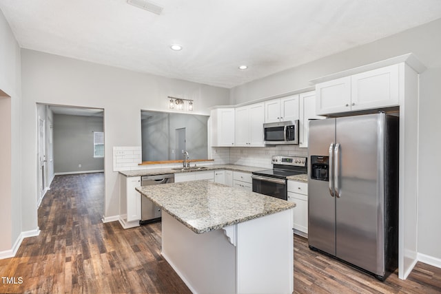 kitchen with appliances with stainless steel finishes, light stone counters, sink, white cabinets, and a kitchen island