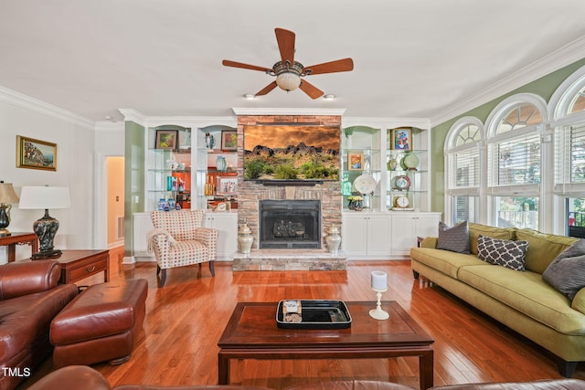 living room featuring ceiling fan, crown molding, a stone fireplace, and hardwood / wood-style floors