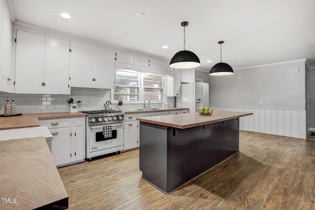 kitchen with high end stove, white fridge with ice dispenser, decorative light fixtures, butcher block counters, and white cabinets