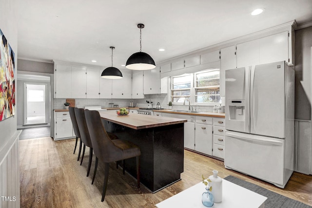 kitchen featuring white cabinetry, white fridge with ice dispenser, decorative light fixtures, and wood counters