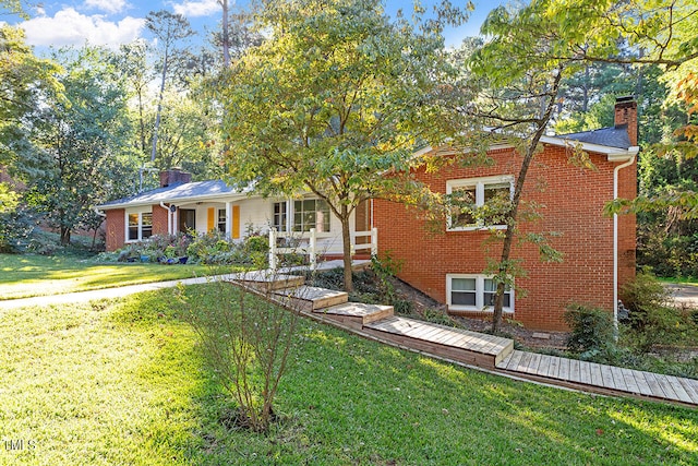 single story home featuring a porch, brick siding, a chimney, and a front yard