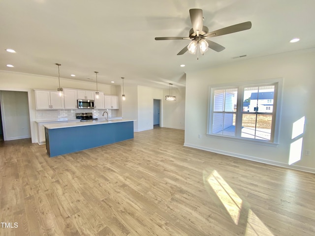 kitchen featuring stainless steel appliances, white cabinets, tasteful backsplash, pendant lighting, and a kitchen island with sink