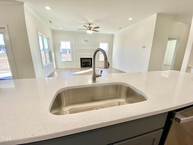 kitchen featuring sink, a large fireplace, crown molding, and light stone counters