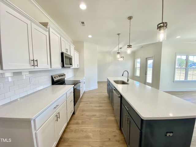 kitchen with a kitchen island with sink, appliances with stainless steel finishes, pendant lighting, white cabinetry, and tasteful backsplash