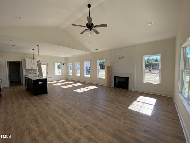 unfurnished living room with dark wood-style flooring, lofted ceiling with beams, a large fireplace, a sink, and baseboards