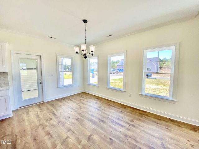 unfurnished dining area featuring crown molding, light wood-style flooring, a notable chandelier, and baseboards
