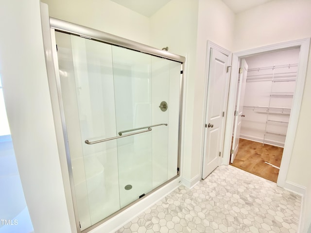 bathroom featuring a spacious closet, baseboards, and a stall shower