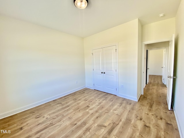 unfurnished bedroom featuring a closet, baseboards, and light wood finished floors