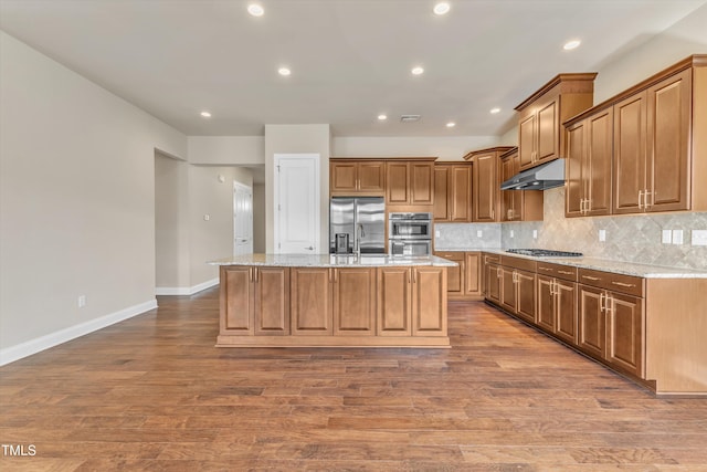 kitchen with light stone counters, a center island with sink, stainless steel appliances, and wood-type flooring