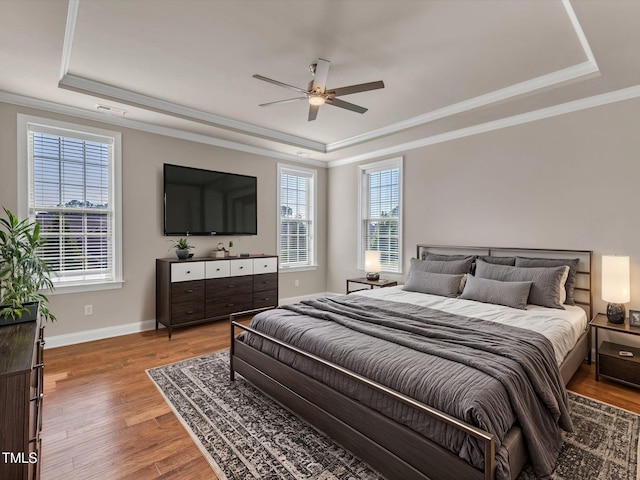 bedroom with hardwood / wood-style flooring, a raised ceiling, ceiling fan, and ornamental molding