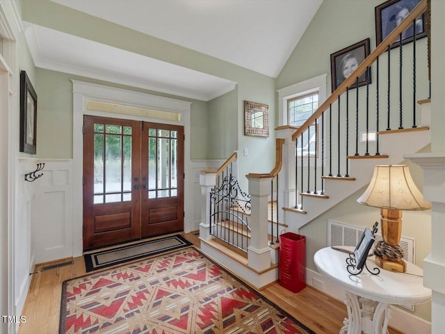 foyer entrance with ornamental molding, hardwood / wood-style floors, vaulted ceiling, and french doors