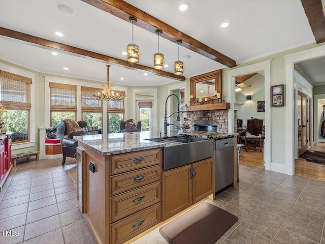 kitchen with an island with sink, hanging light fixtures, sink, stainless steel dishwasher, and light stone counters