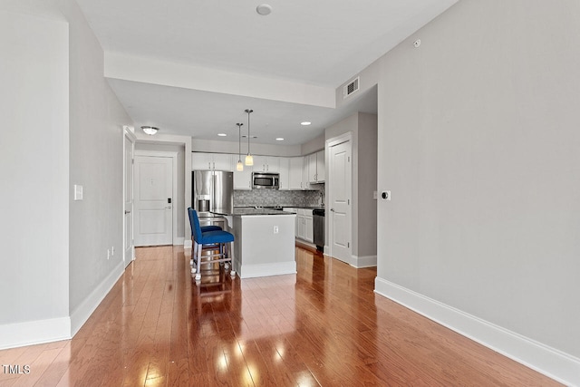 kitchen with a breakfast bar, decorative light fixtures, a center island, stainless steel appliances, and white cabinets