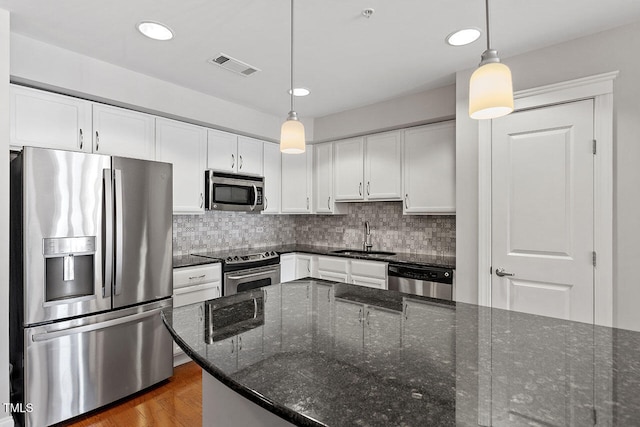 kitchen featuring sink, white cabinetry, appliances with stainless steel finishes, pendant lighting, and dark stone counters