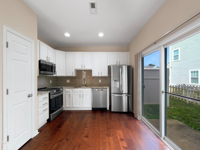 kitchen with dark wood-type flooring, light stone counters, decorative backsplash, white cabinets, and appliances with stainless steel finishes