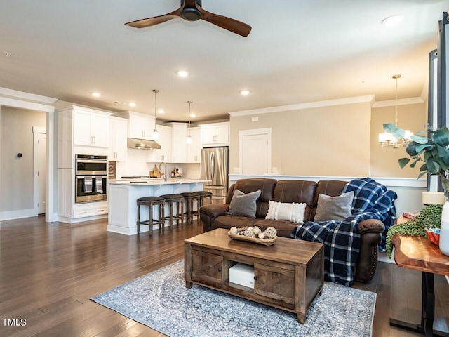 living room with dark wood-type flooring, ceiling fan with notable chandelier, and ornamental molding