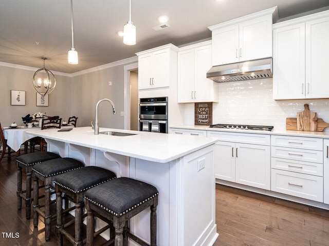 kitchen with an island with sink, decorative light fixtures, sink, and white cabinetry