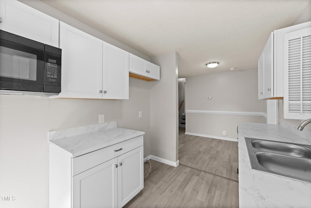 kitchen featuring light stone counters, white cabinets, sink, and light hardwood / wood-style floors