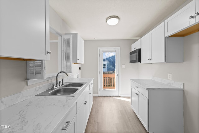 kitchen with sink, a textured ceiling, light hardwood / wood-style flooring, white cabinetry, and light stone countertops