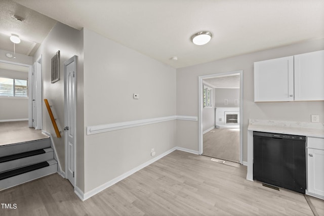 kitchen with a textured ceiling, black dishwasher, light hardwood / wood-style flooring, and white cabinets