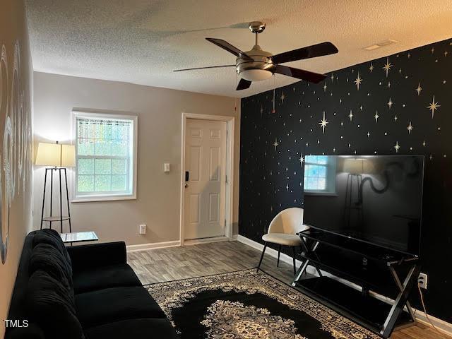 living room with ceiling fan, wood-type flooring, and a textured ceiling