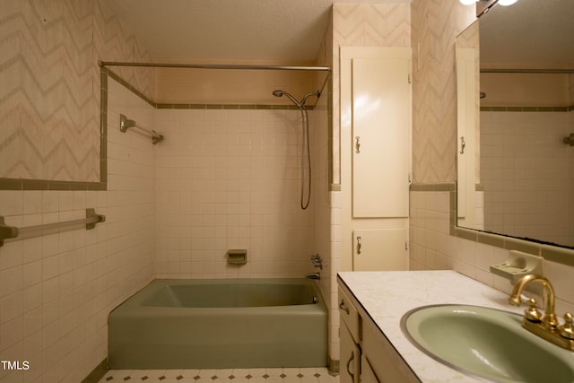 bathroom with tile walls, vanity, tiled shower / bath, and a textured ceiling