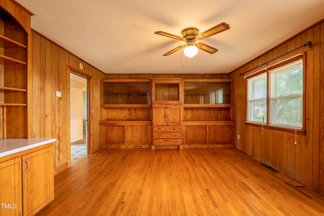 unfurnished living room with ceiling fan, wooden walls, light wood-type flooring, and a textured ceiling