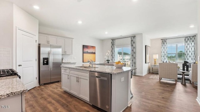 kitchen featuring light stone counters, an island with sink, sink, stainless steel appliances, and dark hardwood / wood-style flooring