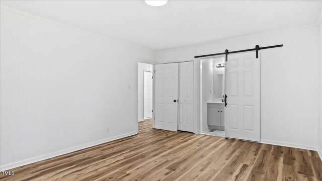 unfurnished bedroom with hardwood / wood-style floors, a closet, connected bathroom, a barn door, and ornamental molding