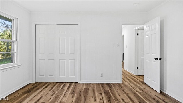 unfurnished bedroom featuring hardwood / wood-style flooring, crown molding, and a closet