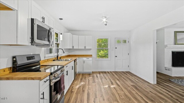 kitchen with butcher block countertops, white cabinetry, sink, and stainless steel appliances