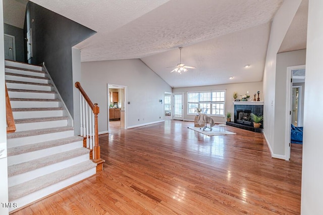 unfurnished living room featuring lofted ceiling, ceiling fan, light wood-type flooring, a textured ceiling, and a tiled fireplace