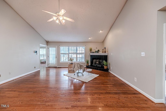 living room featuring a fireplace, wood-type flooring, vaulted ceiling, and ceiling fan