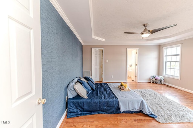 bedroom with ensuite bath, ceiling fan, a raised ceiling, crown molding, and hardwood / wood-style floors