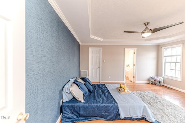 bedroom with ensuite bathroom, a raised ceiling, hardwood / wood-style flooring, ceiling fan, and ornamental molding