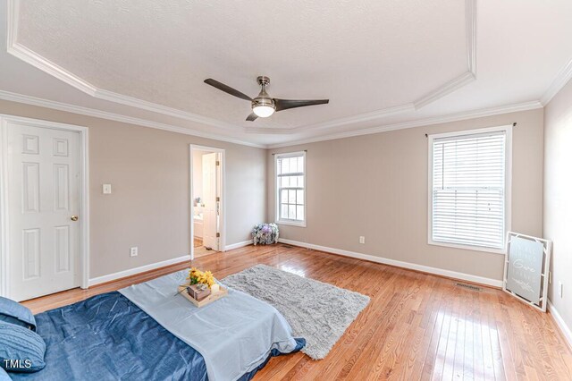 bedroom featuring ornamental molding, a tray ceiling, ceiling fan, multiple windows, and light hardwood / wood-style floors