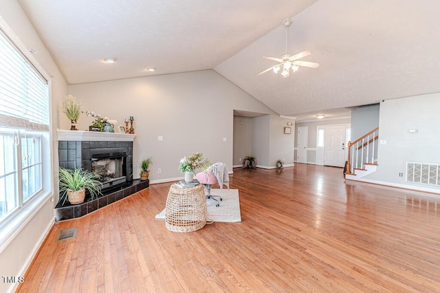 living room featuring a tiled fireplace, a healthy amount of sunlight, vaulted ceiling, and light hardwood / wood-style floors