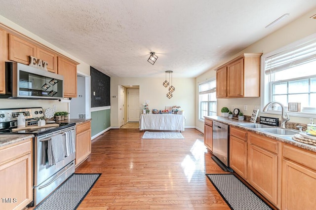 kitchen featuring hanging light fixtures, sink, a textured ceiling, appliances with stainless steel finishes, and light hardwood / wood-style floors