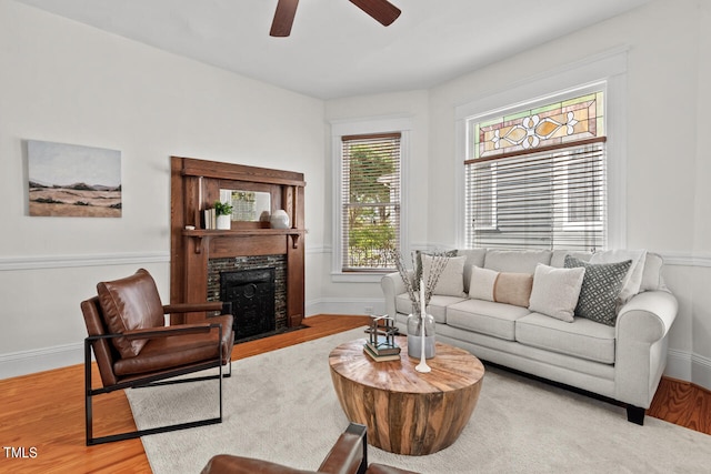 living room with light hardwood / wood-style floors, a stone fireplace, and ceiling fan